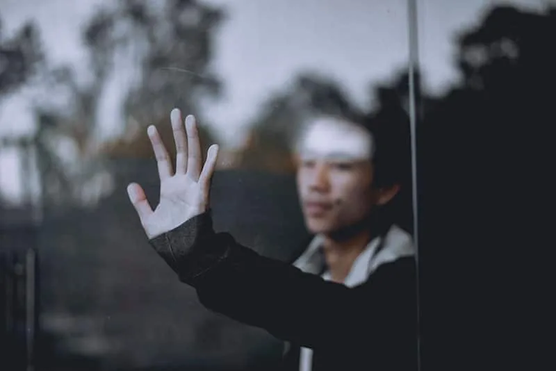 Person with a hand pressed against a rain-covered window