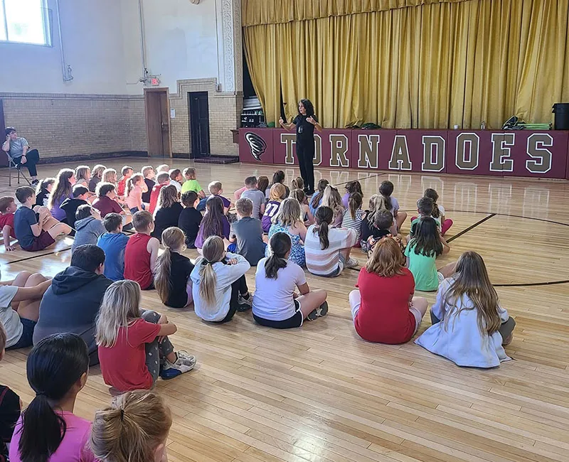 Students seated on a gym floor during Jodee Blanco’s presentation
